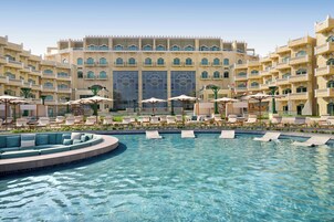A hotel with a large pool, multiple lounge areas, and a grand building facade.