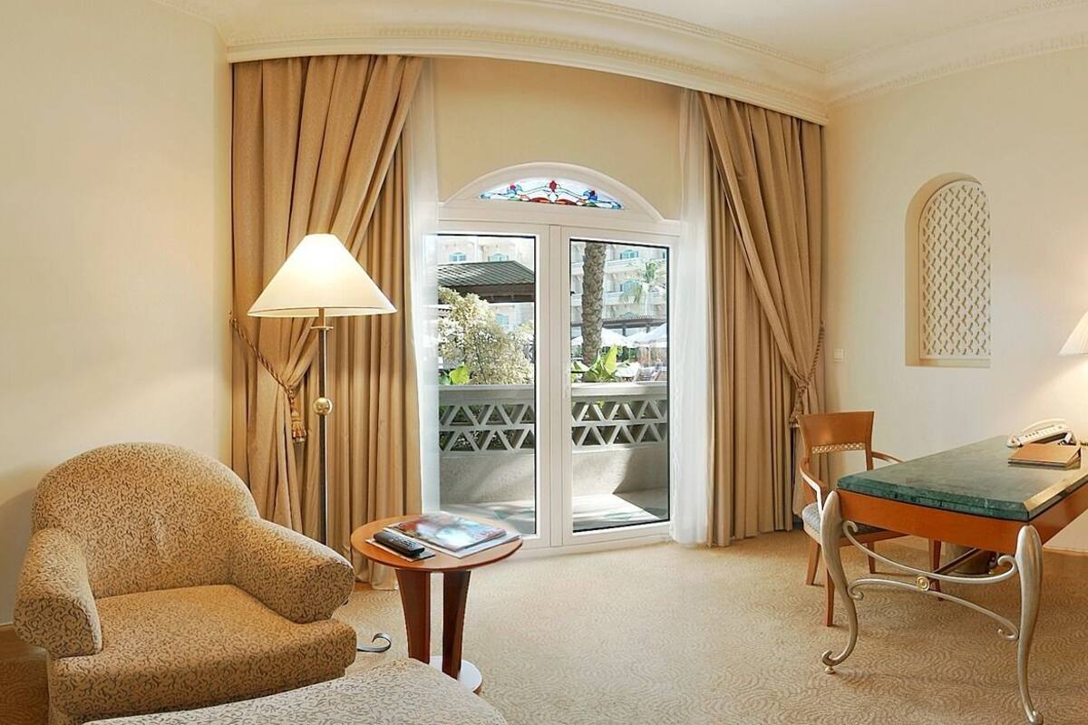 Quarto de hotel com uma cama grande, uma escrivaninha, uma cadeira, um guarda-roupa e vista para o exterior.