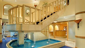 Una piscina amplia en el interior con una escalera de mármol y una zona de recepción.