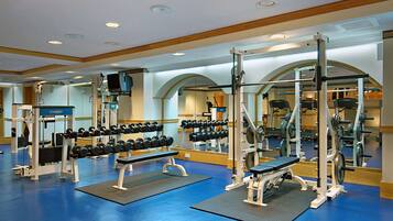 A gym with weightlifting equipment, mirrors, and blue flooring.
