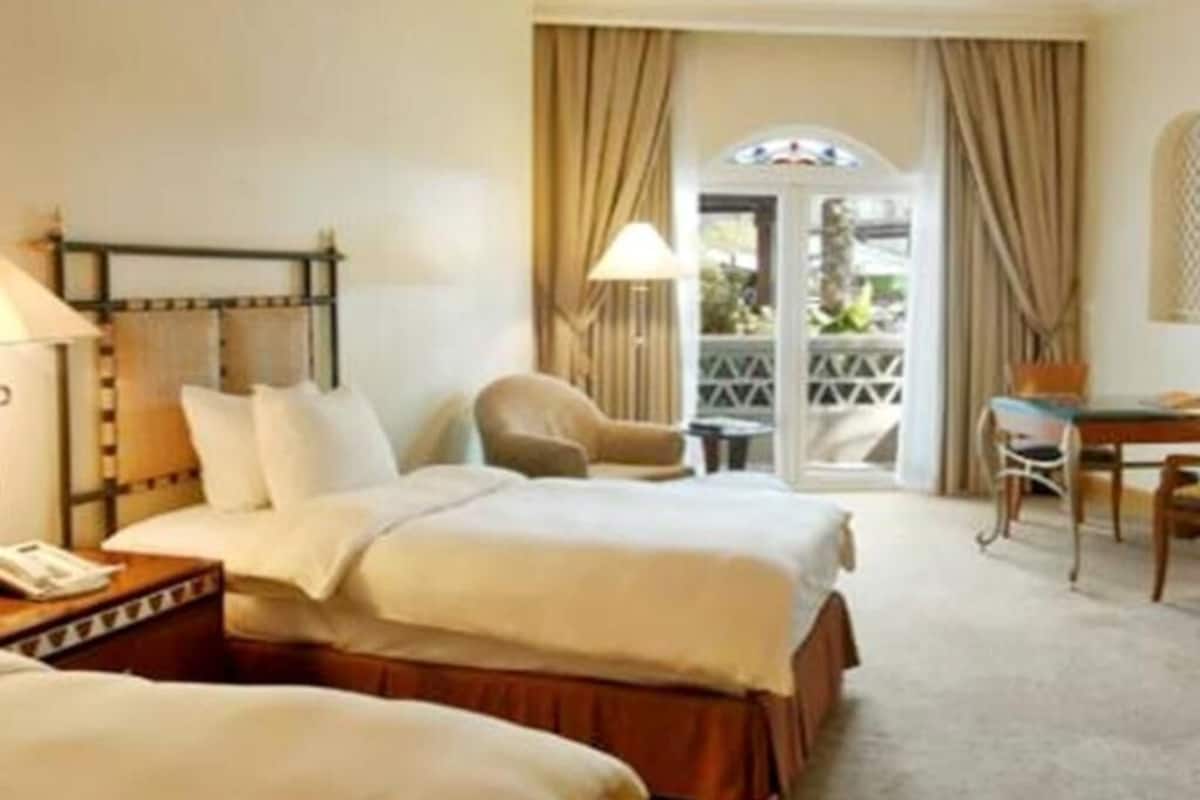 A hotel room with two beds, a desk, a chair, and a balcony with curtains.