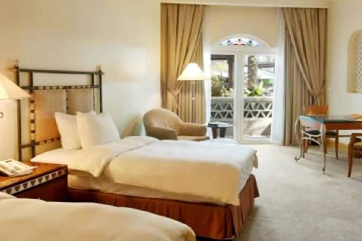 Quarto de hotel com cama, escrivaninha, cadeira e janela com cortinas.