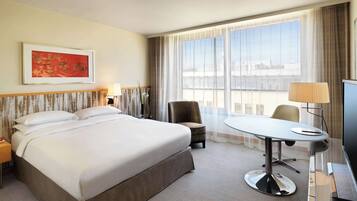 Une chambre d’hôtel avec un grand lit, un bureau avec une chaise, une télévision et une fenêtre avec des rideaux.