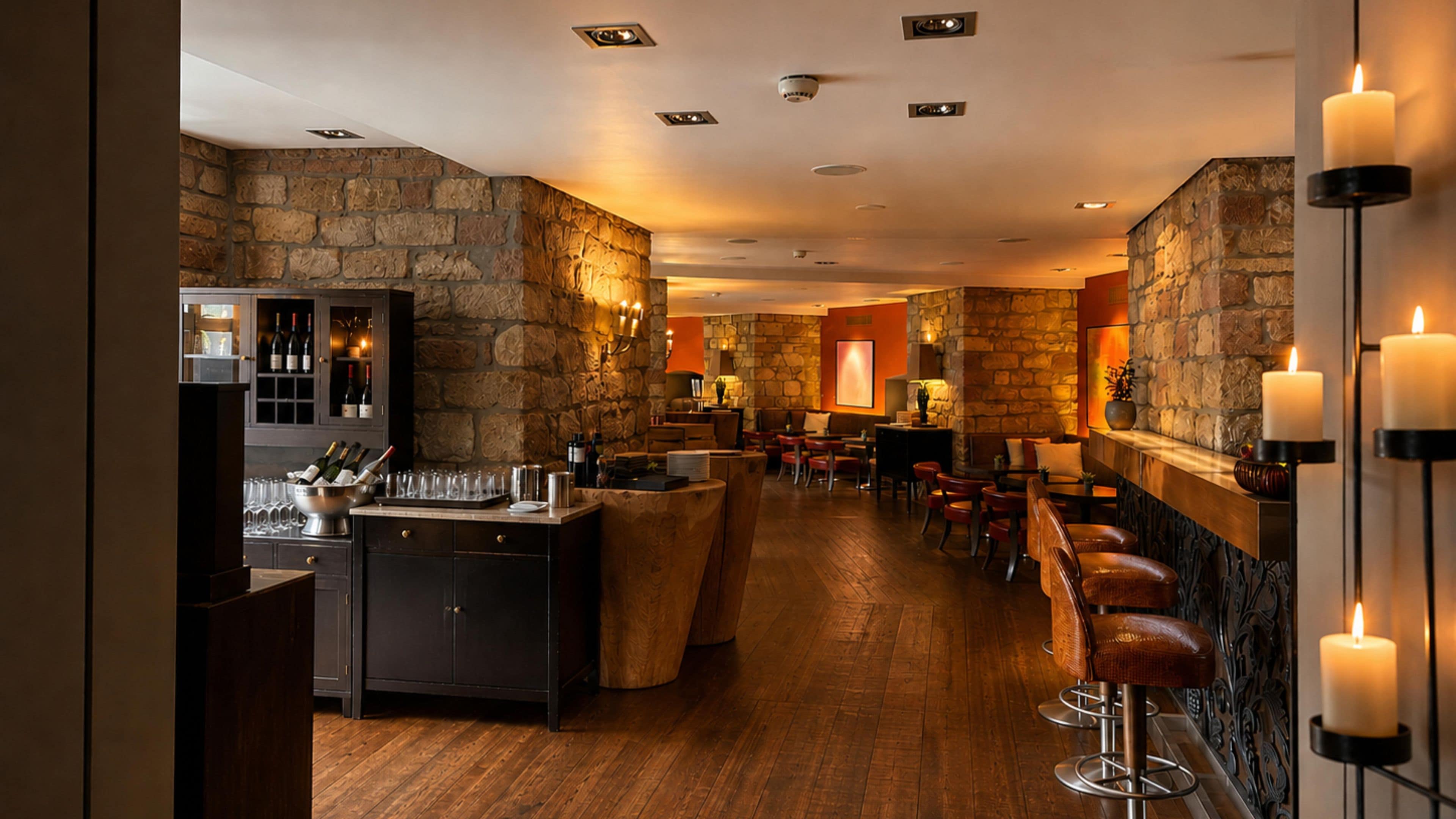 A bar area with a stone wall backdrop, wooden flooring, and multiple bar stools.