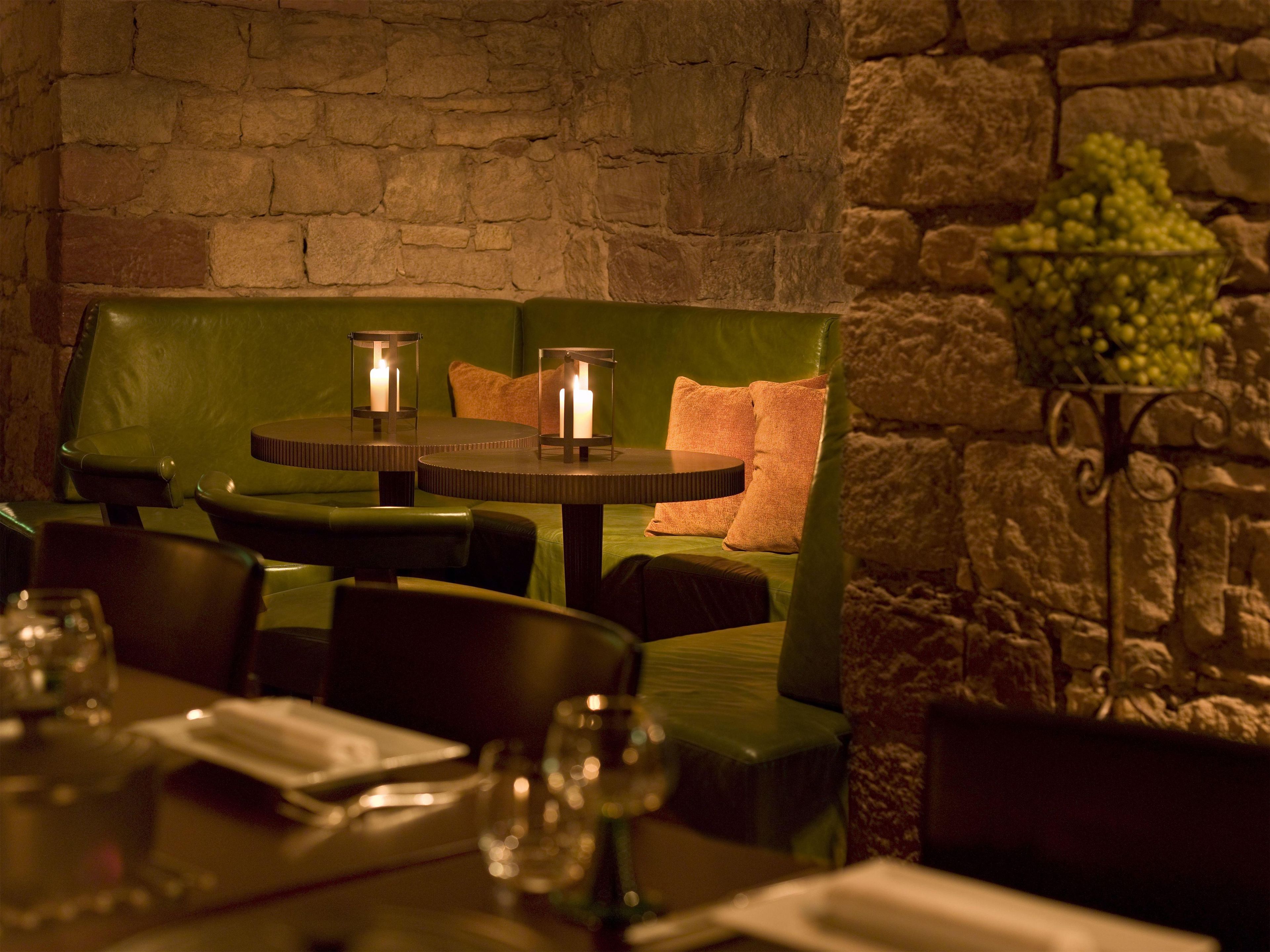 A restaurant interior with stone walls, green upholstered seating, and candle-lit tables.