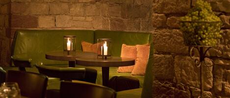 A restaurant interior with stone walls, green upholstered seating, and candle-lit tables.