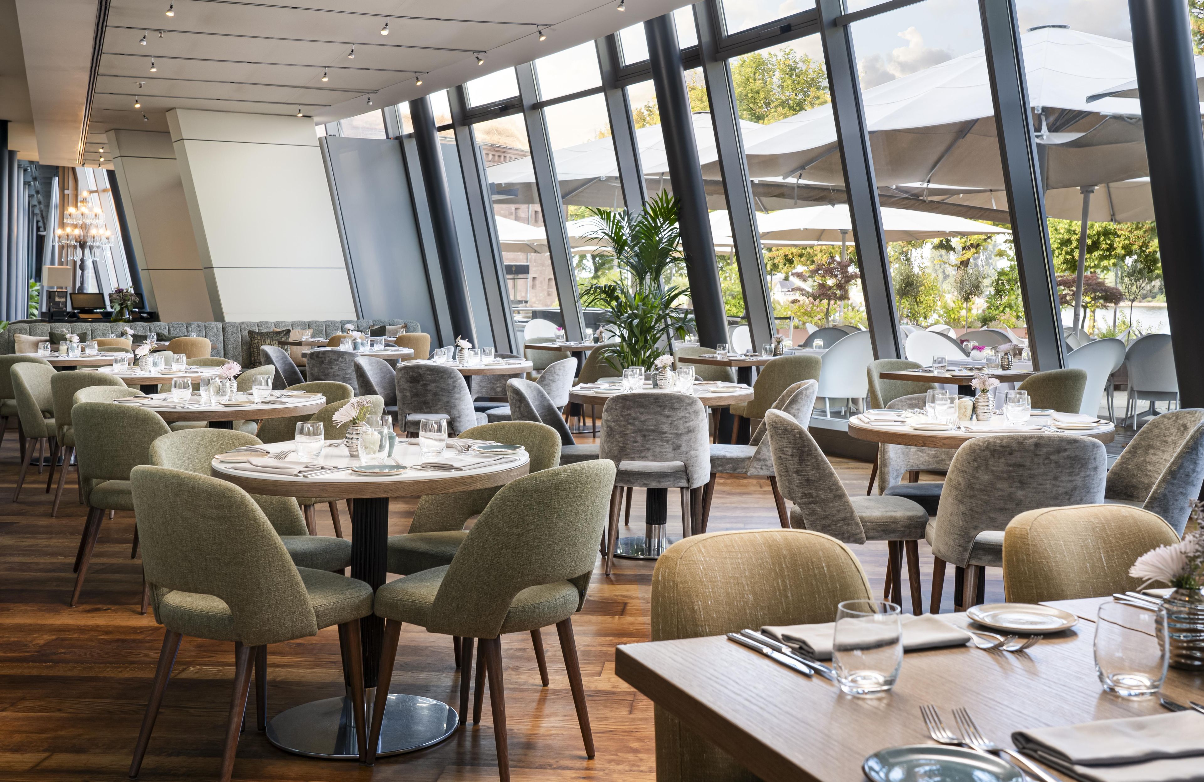 A restaurant with round tables and chairs, large windows, and a view of the outdoors.
