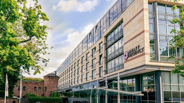 A modern hotel with a glass facade, a brick building in the background, and a clear sky.