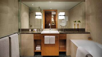 A modern bathroom with a large mirror, a sink, and a bathtub. There are towels and toiletries on the counter.