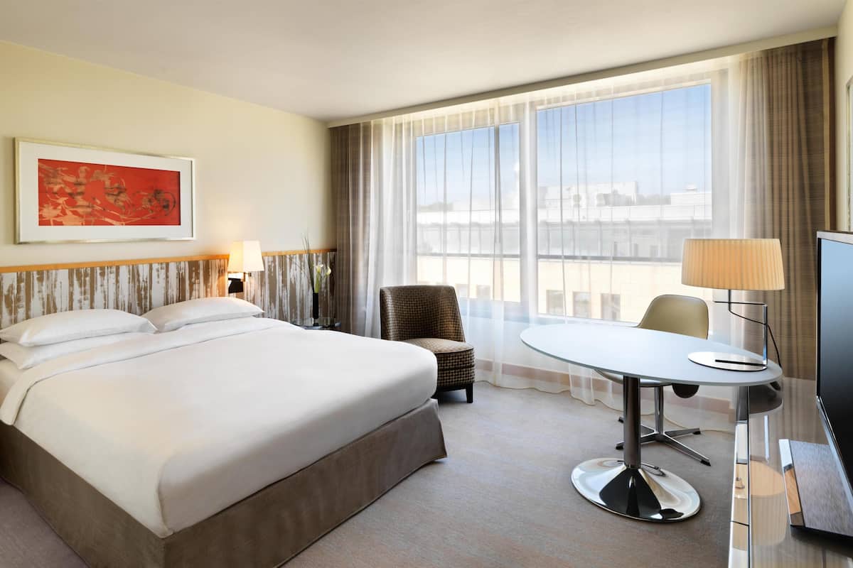 A hotel room with a large bed, a desk with a chair, a television, and a window with curtains.