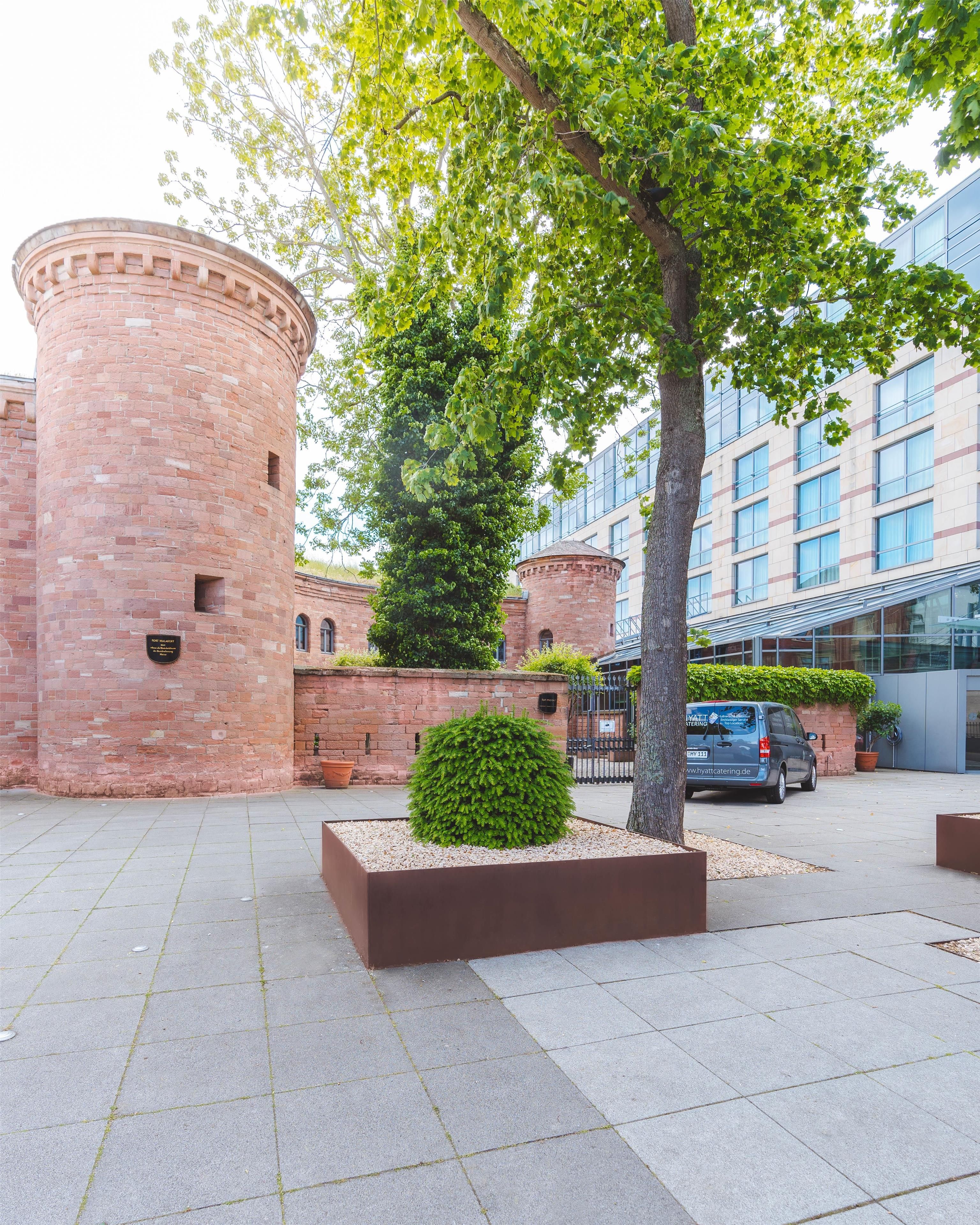 Un patio con una torre de ladrillo, un árbol grande y un edificio moderno con ventanales de vidrio.