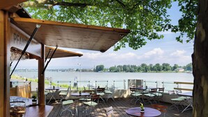 An outdoor terrace with tables and chairs, overlooking a body of water. - Hyatt Regency Mainz (Mainz)