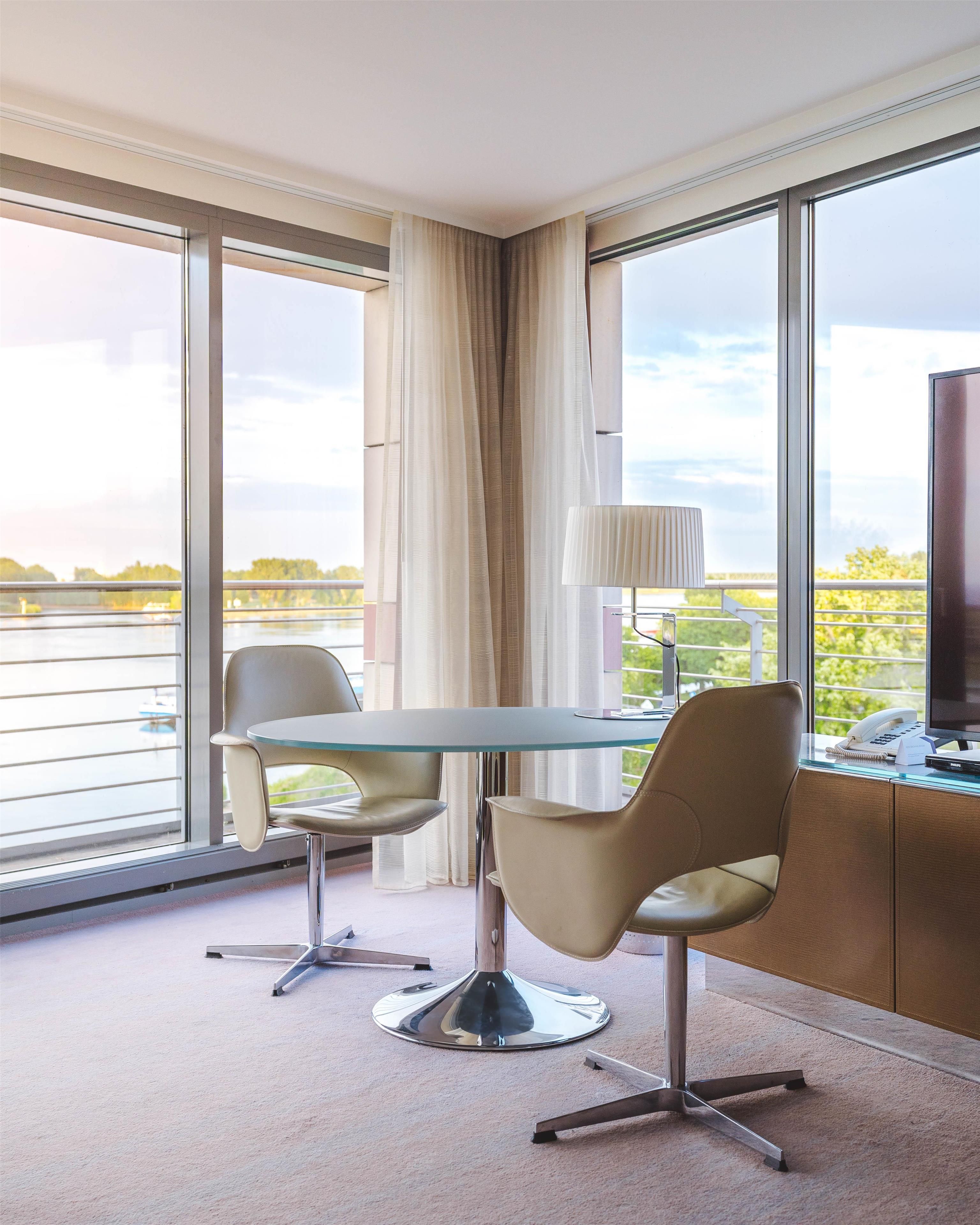 Une chambre d’hôtel avec une table en verre, deux chaises, une lampe, un téléphone et un téléviseur.