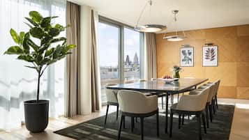 Un comedor moderno con una mesa grande, sillas, una planta en maceta y vistas a la ciudad a través de amplios ventanales.