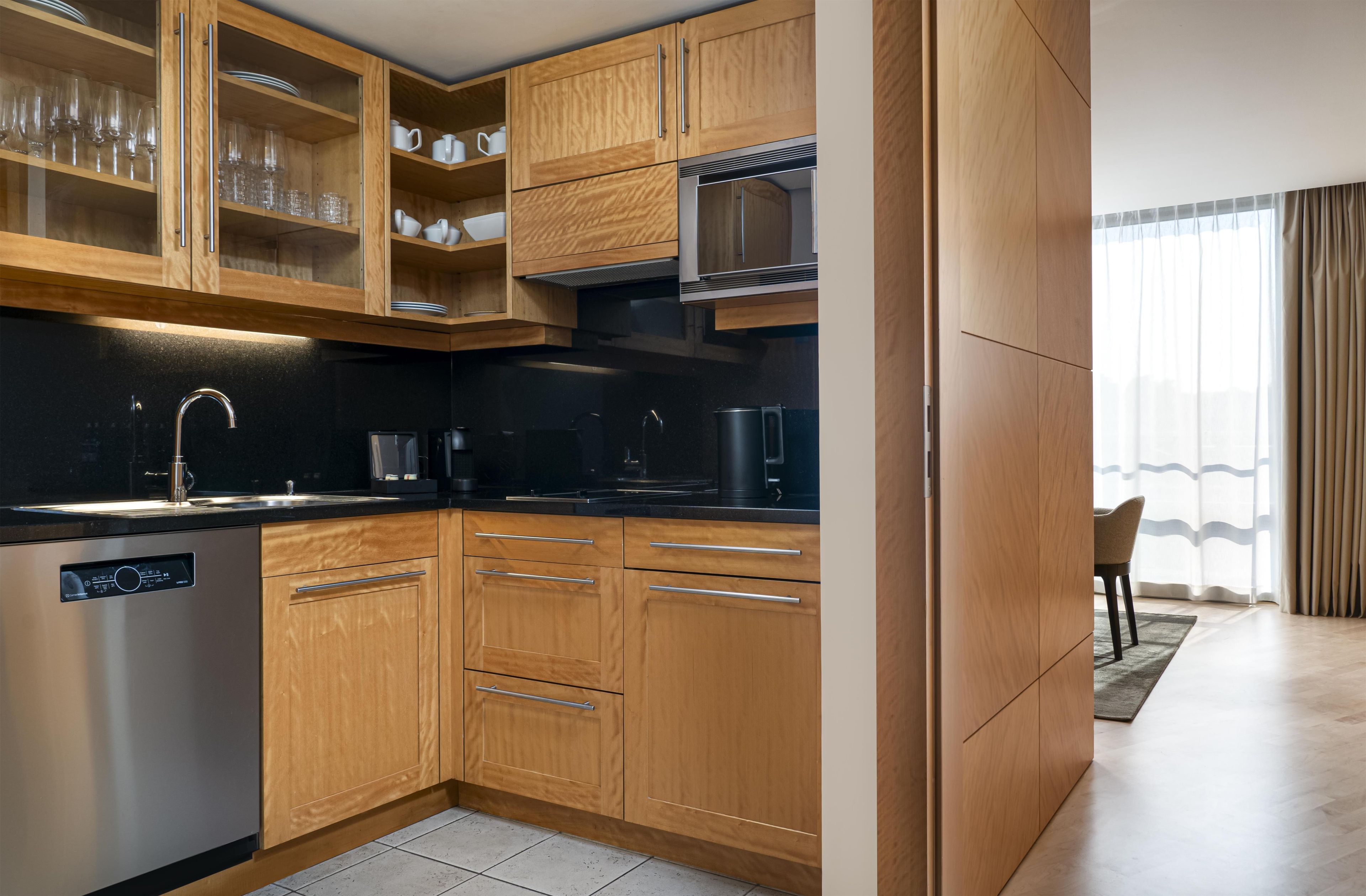 A modern kitchen with wooden cabinets, a stainless steel dishwasher, and a black countertop.
