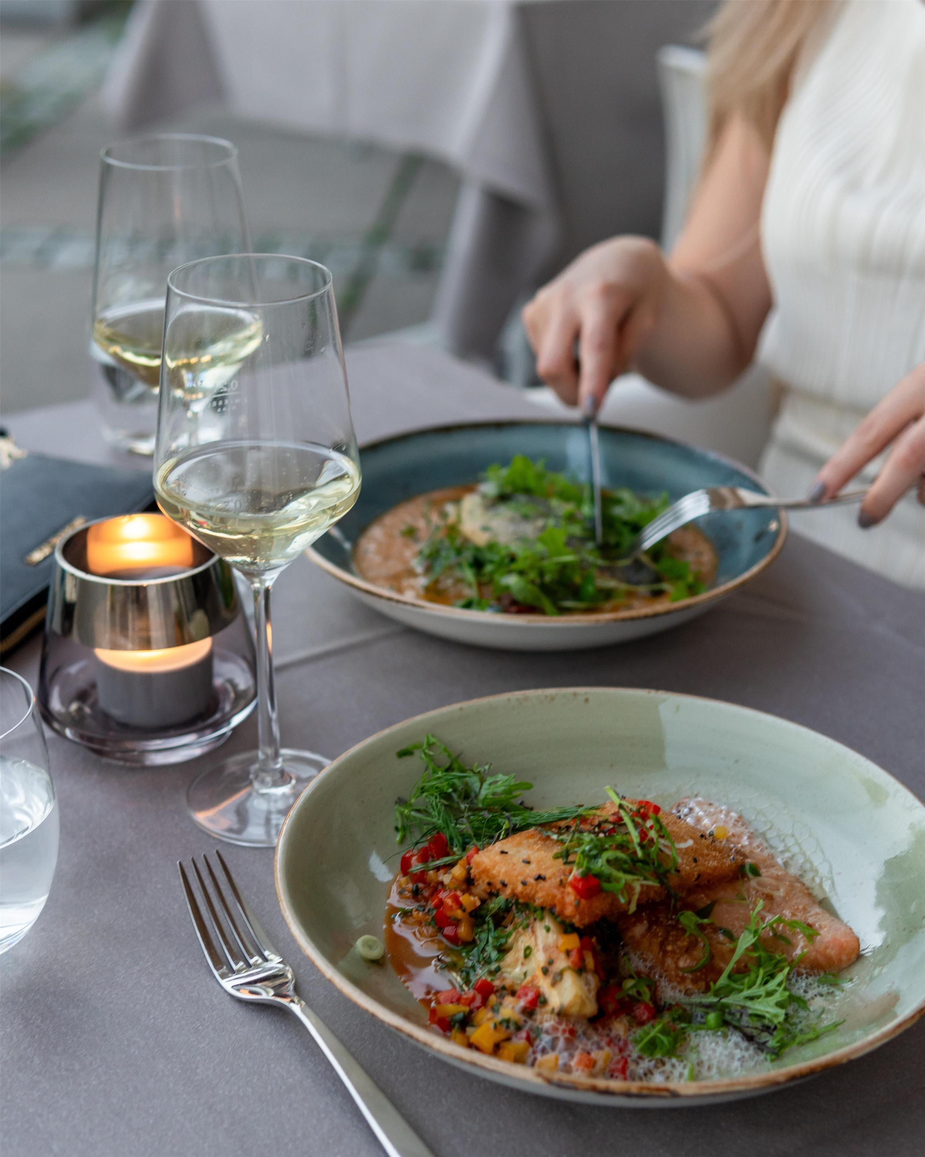 A dining table with a candle, wine glasses, and a plate of food.