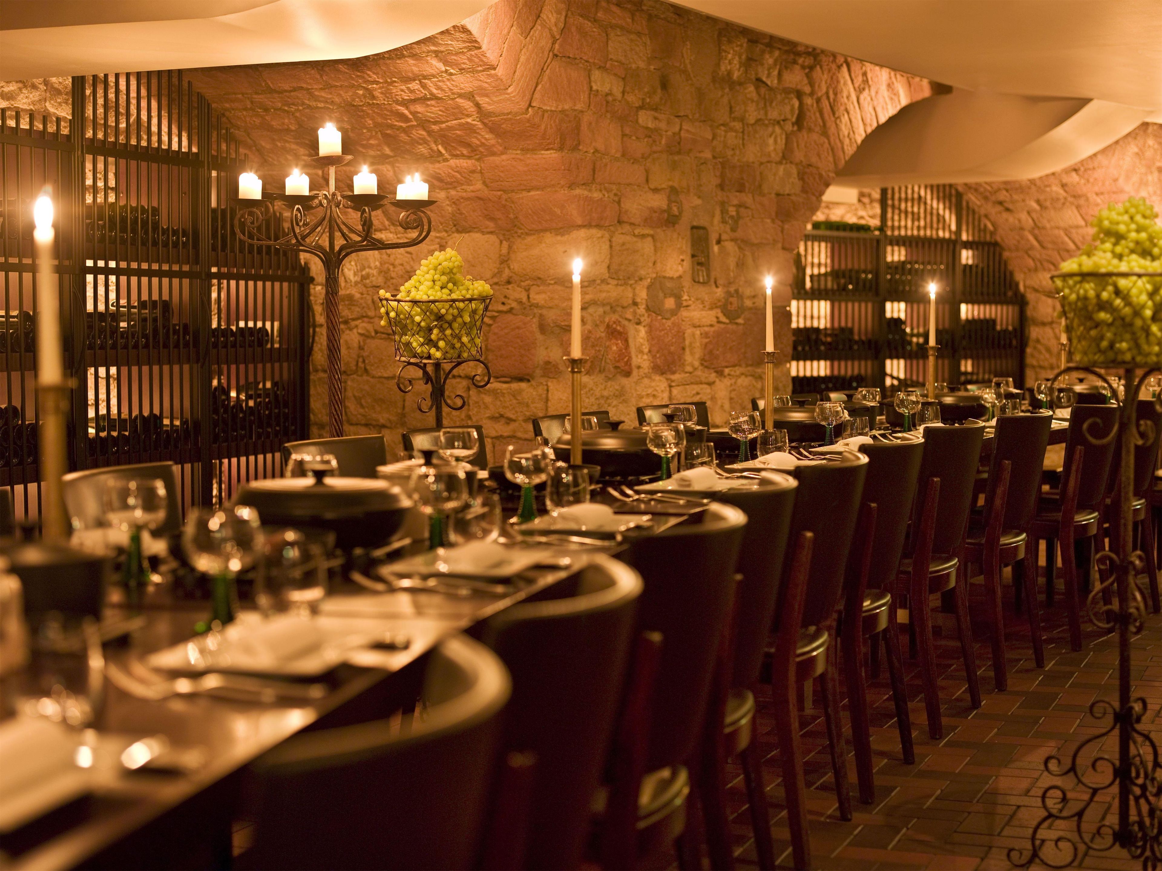 Un restaurante con pared de piedra, mesas iluminadas por velas y una estantería para vinos.
