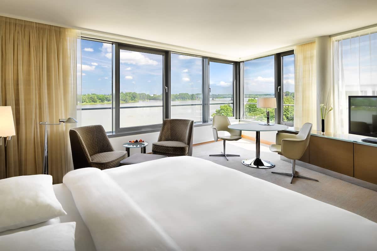 A hotel room with a large bed, two armchairs, a small table, and a TV.