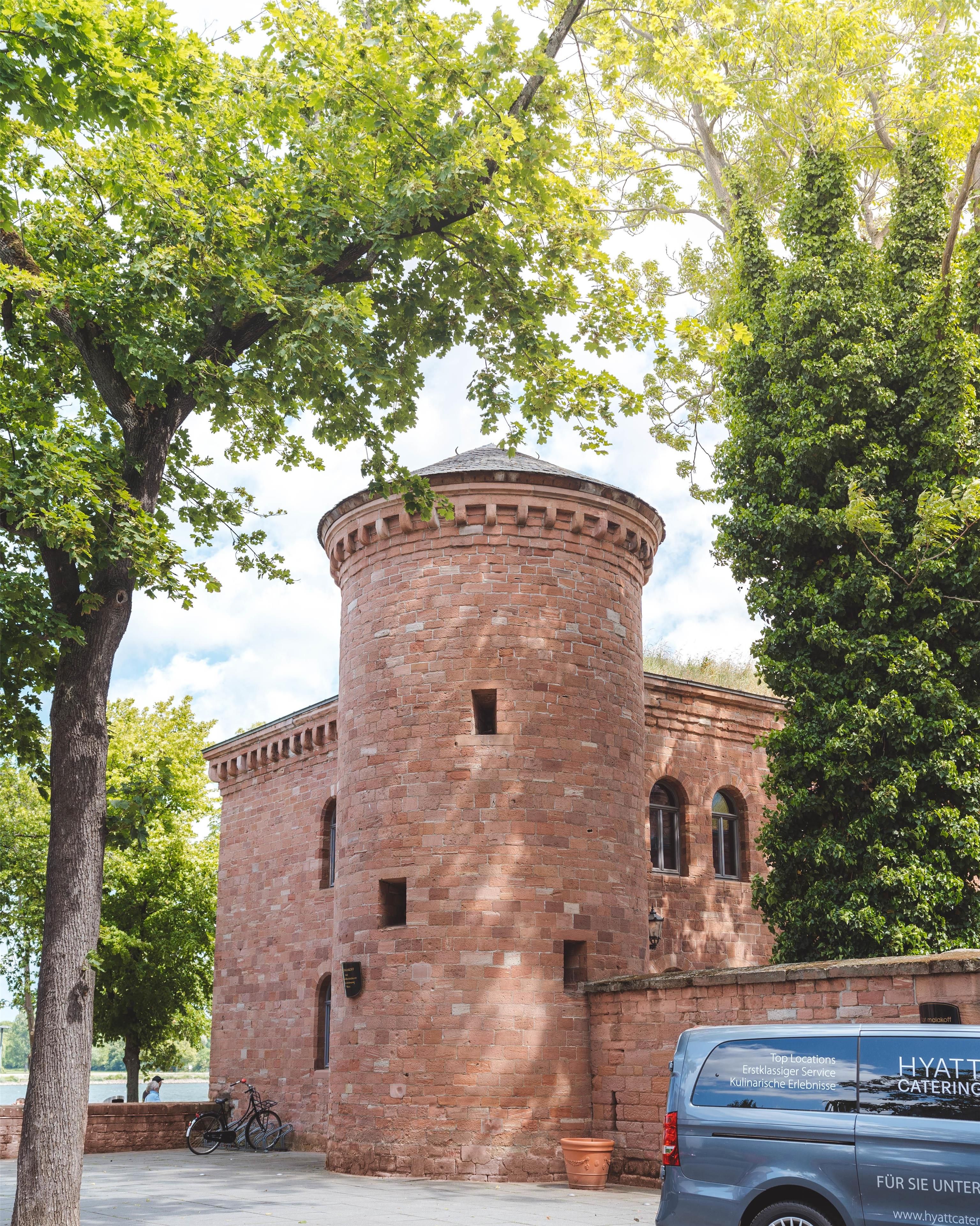 A historic brick building with a round tower, a bicycle parked in front, and a car with a visible advertisement.
