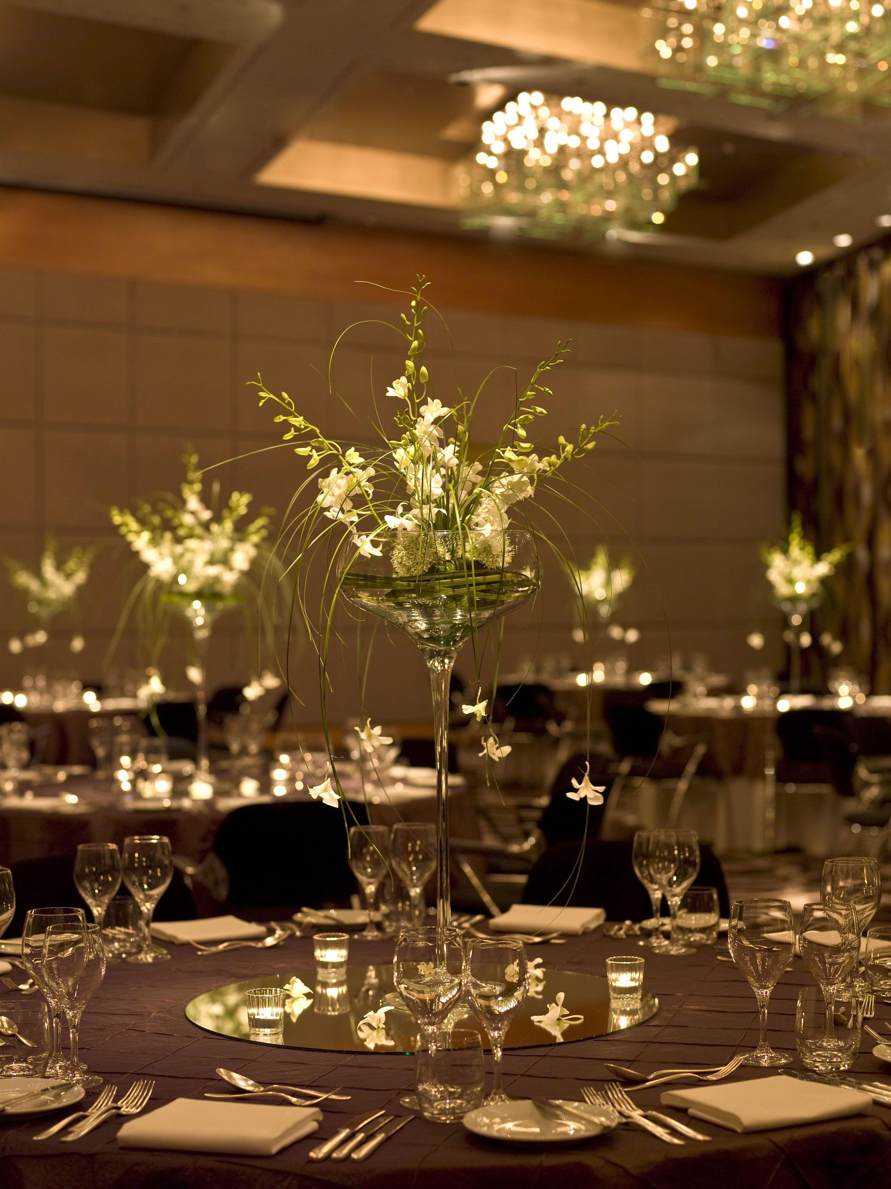 Una mesa de comedor con varios vasos de vino, tenedores y un centro de mesa con flores blancas en un jarrón de vidrio.
