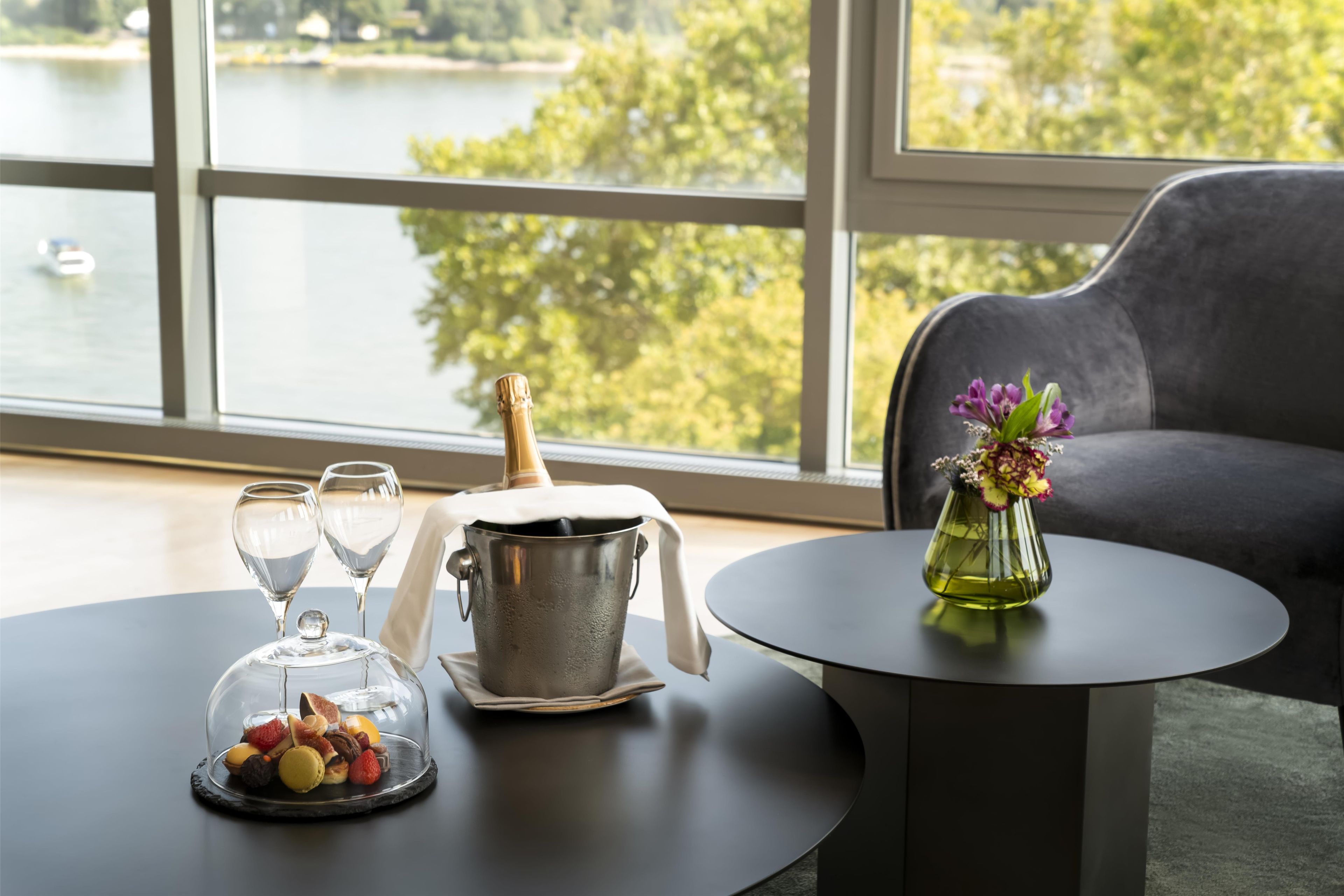 A table with a champagne bottle, two glasses, a fruit platter, and a vase with flowers.