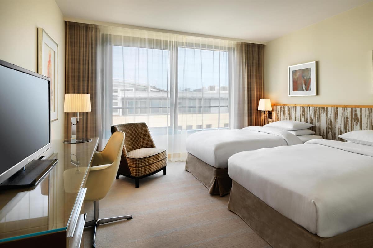 A hotel room with a bed, a desk, a chair, a TV, and a window with curtains.