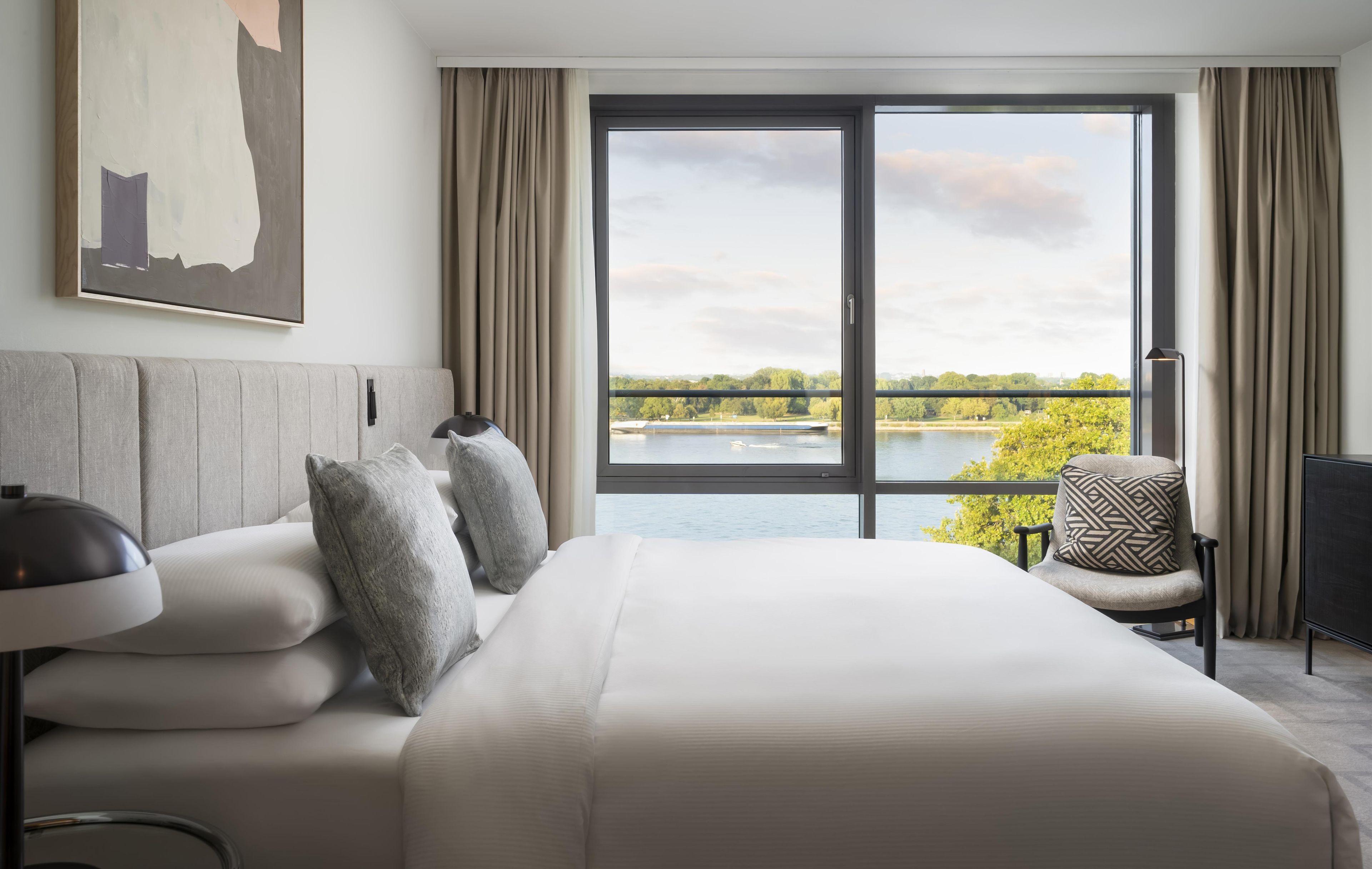 Habitación de hotel con una cama grande, una silla, un escritorio y vistas a un lago.