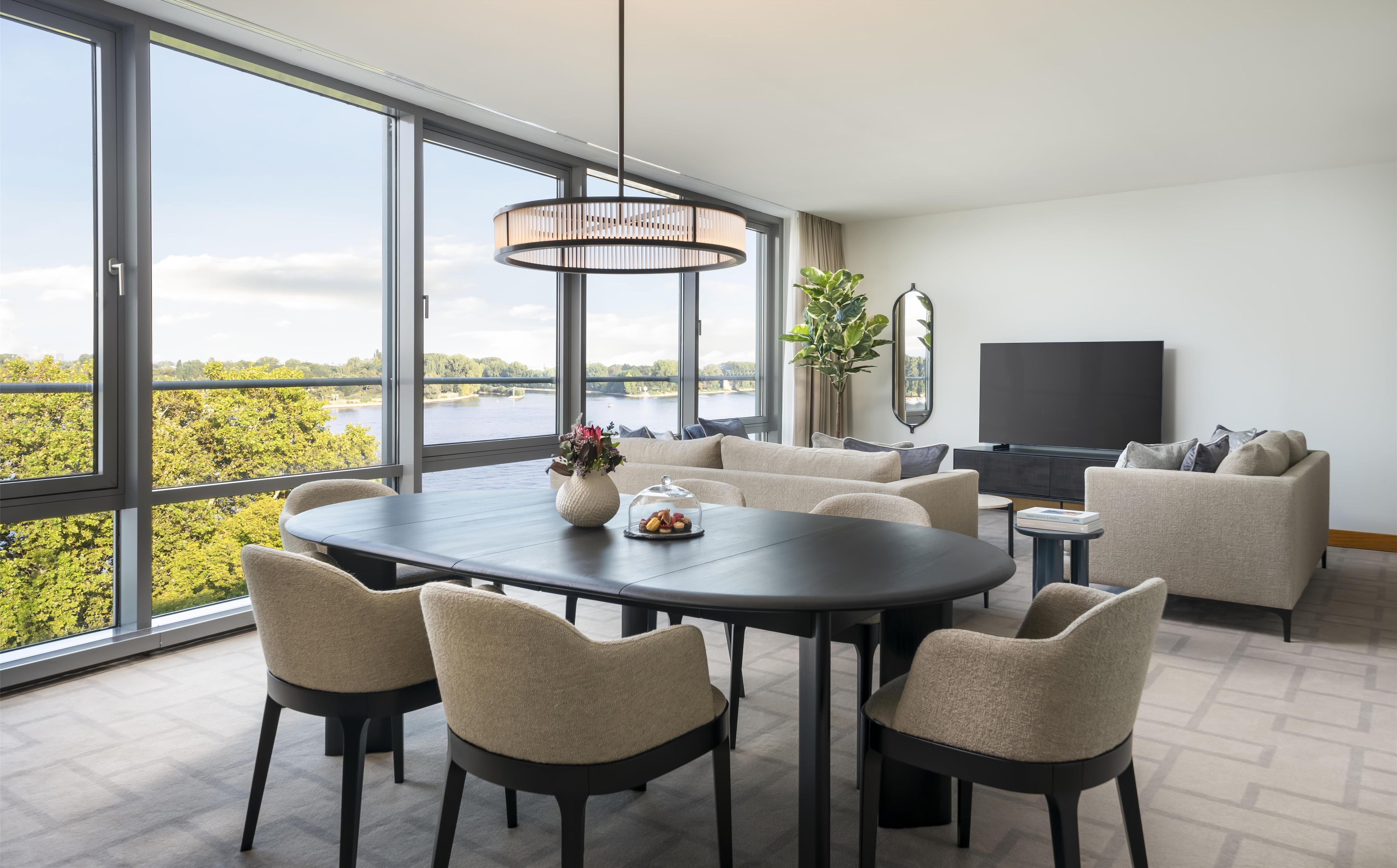 Una sala de estar moderna con comedor, ventanas amplias y vista a un lago.