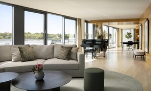 A modern living room with a sofa, a piano, and a view of the outdoors. - Hyatt Regency Mainz (Mainz)