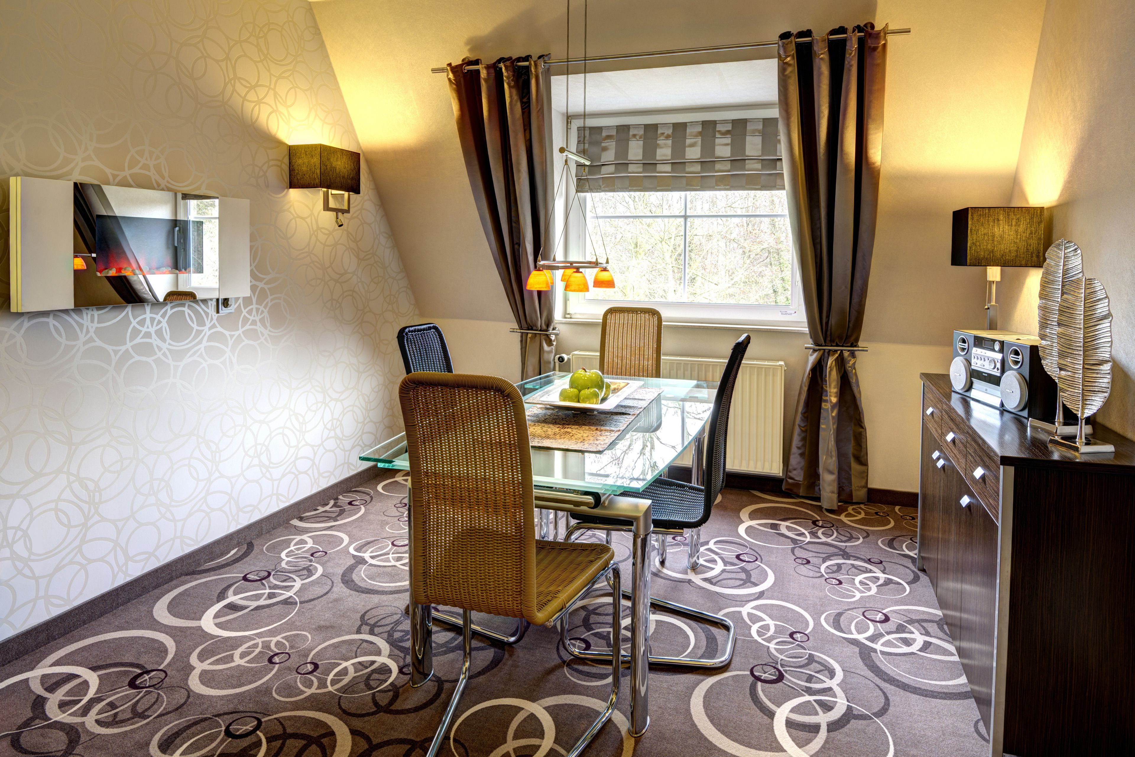 Een eethoek met een glazen tafel, rieten stoelen en uitzicht op de omgeving door een raam met gordijnen.