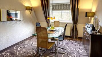 Een eethoek met een glazen tafel, rieten stoelen en uitzicht op de omgeving door een raam met gordijnen.