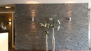 Un área de recepción con una pared de piedra, dos jarrones altos con flores y un mostrador de madera.