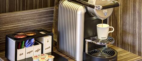 Una cafetera Nespresso con una cafetera de goteo, una taza de café y un portacapsulas con té, azúcar y cápsulas de café.