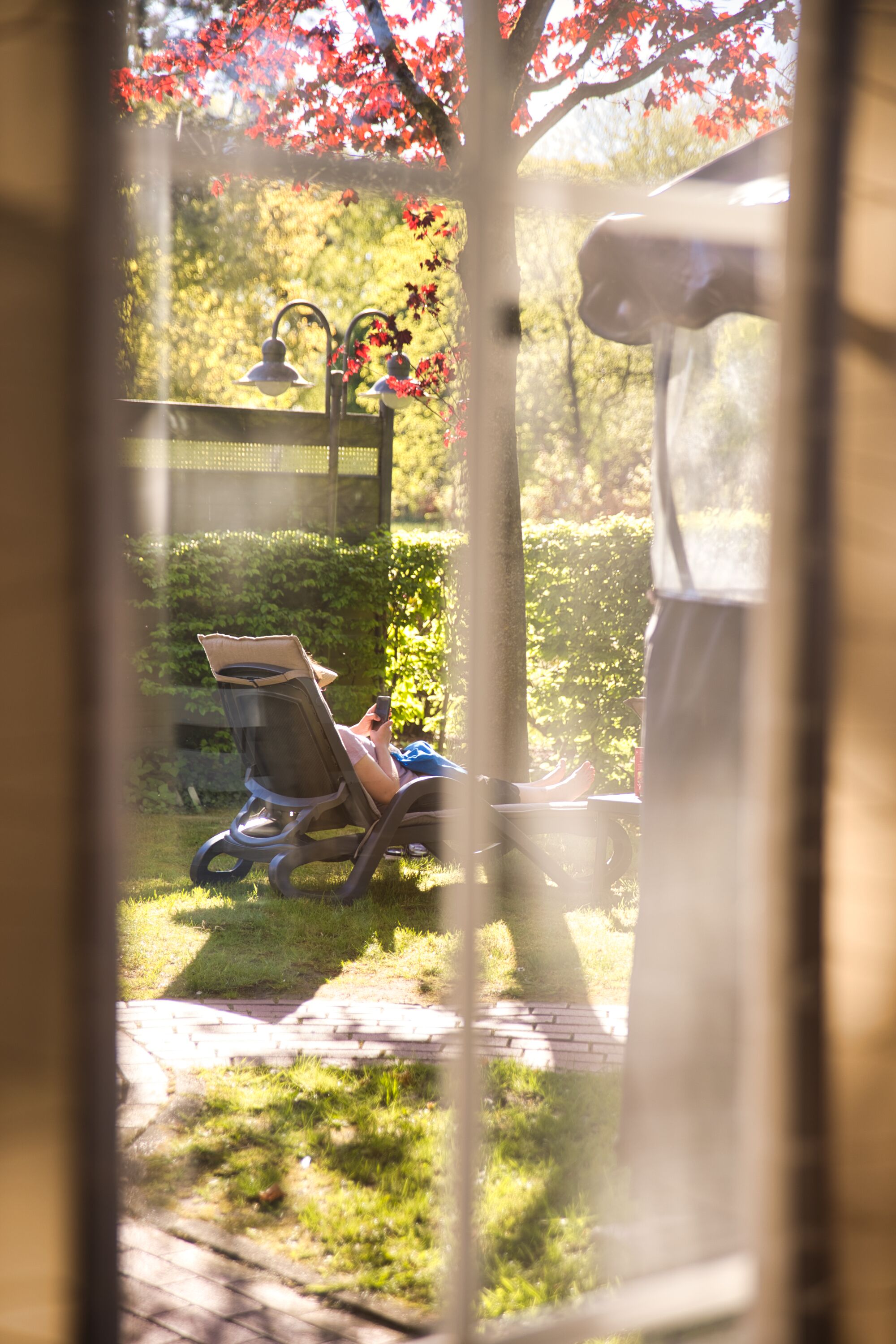 A garden view through a window with a lawn chair, a bench, and a statue.