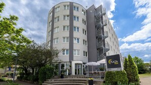 A multi-story hotel with a modern design, featuring a prominent spiral staircase, a covered outdoor seating area, and a sign indicating it is a Plaza Inn.