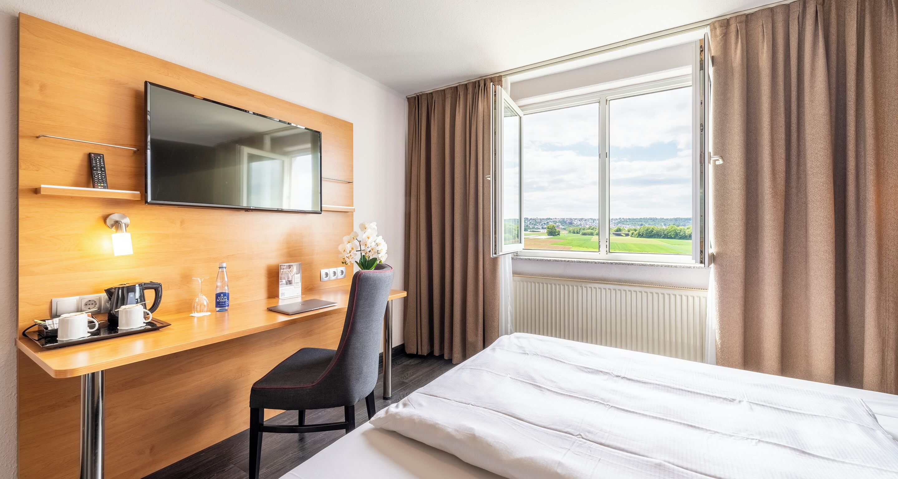 Une chambre d’hôtel avec un lit, un bureau avec une télévision, une chaise et une fenêtre avec des rideaux.