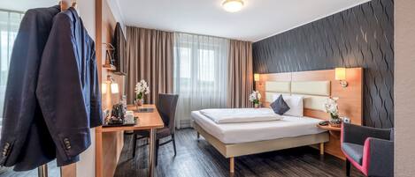 Una habitación de hotel con cama, escritorio, silla y perchero.