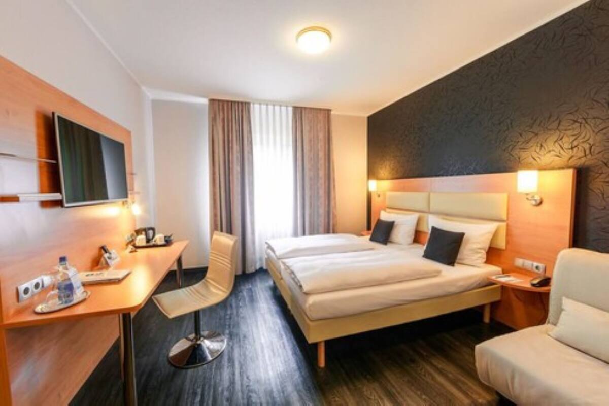 A hotel room with a bed, desk, chair, and a TV.