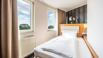 Ein Hotelzimmer mit Bett, Nachttisch, Lampe, Fenster und Blick ins Freie.