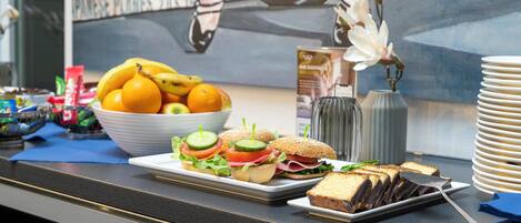 Une table de buffet avec des sandwichs, des fruits et un dessert au chocolat.