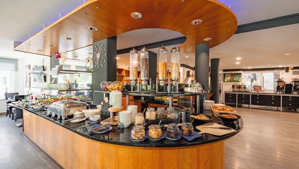 A buffet area with various food items and containers, a clock, and a modern ceiling design.