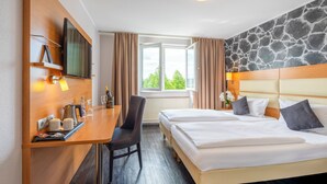 A hotel room with a bed, a desk with a chair, a TV, and a window with curtains.