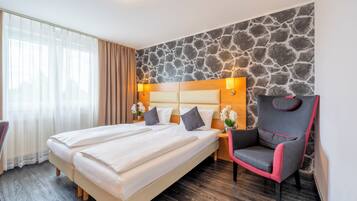 A hotel room with a large bed, a chair, a nightstand, and a stone wall.