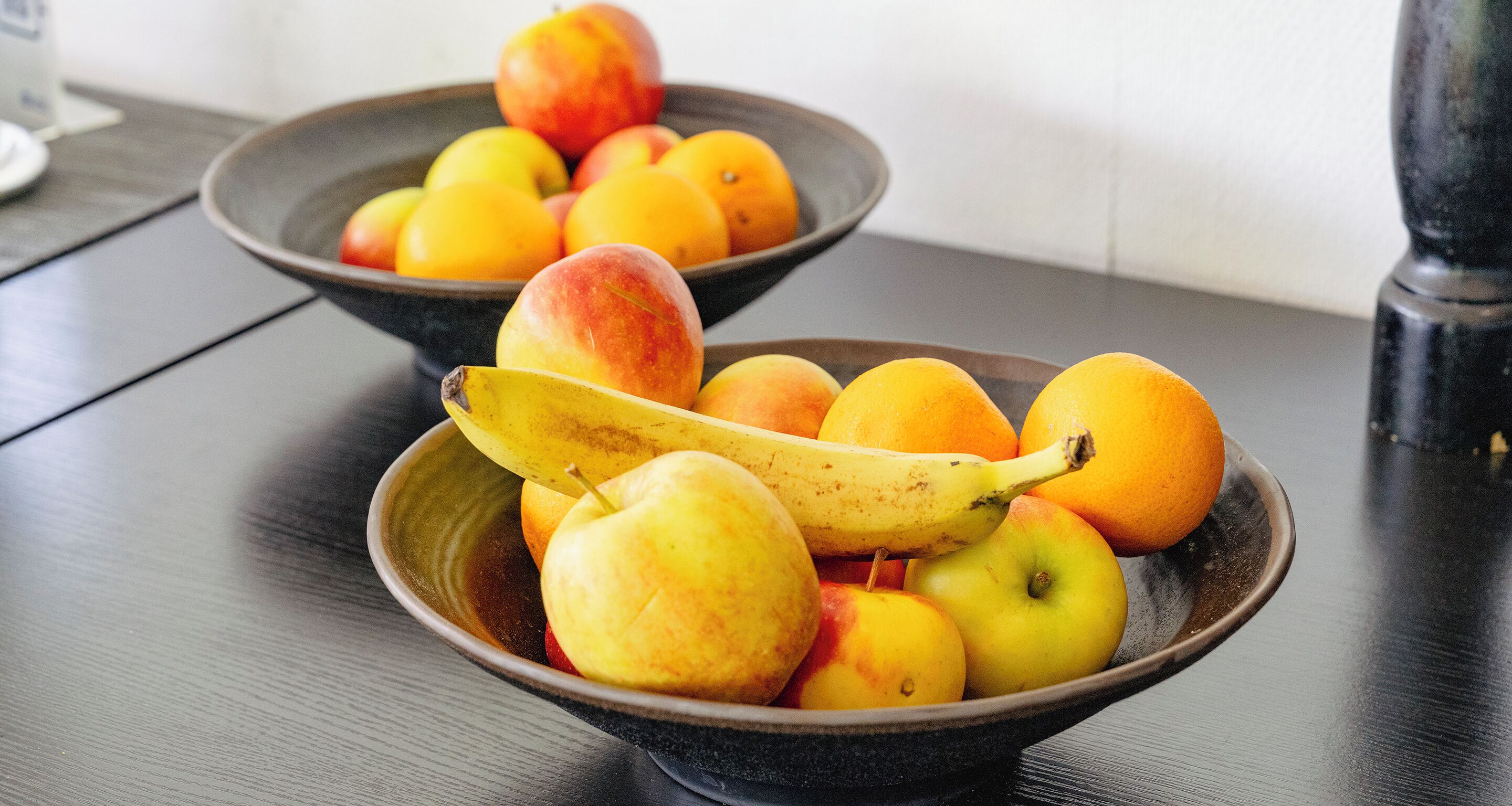 Two bowls of fruit on a dark wooden table.