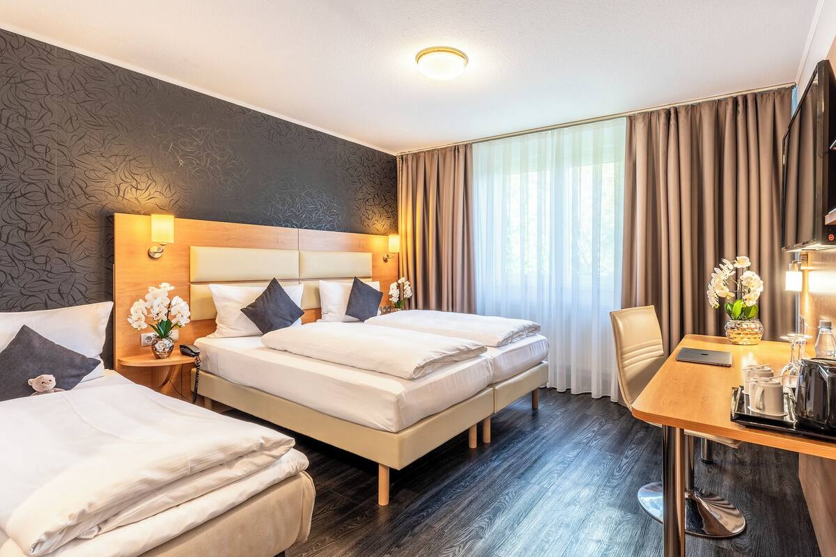 A hotel room with two beds, a desk with a chair, a TV, and a window with curtains.