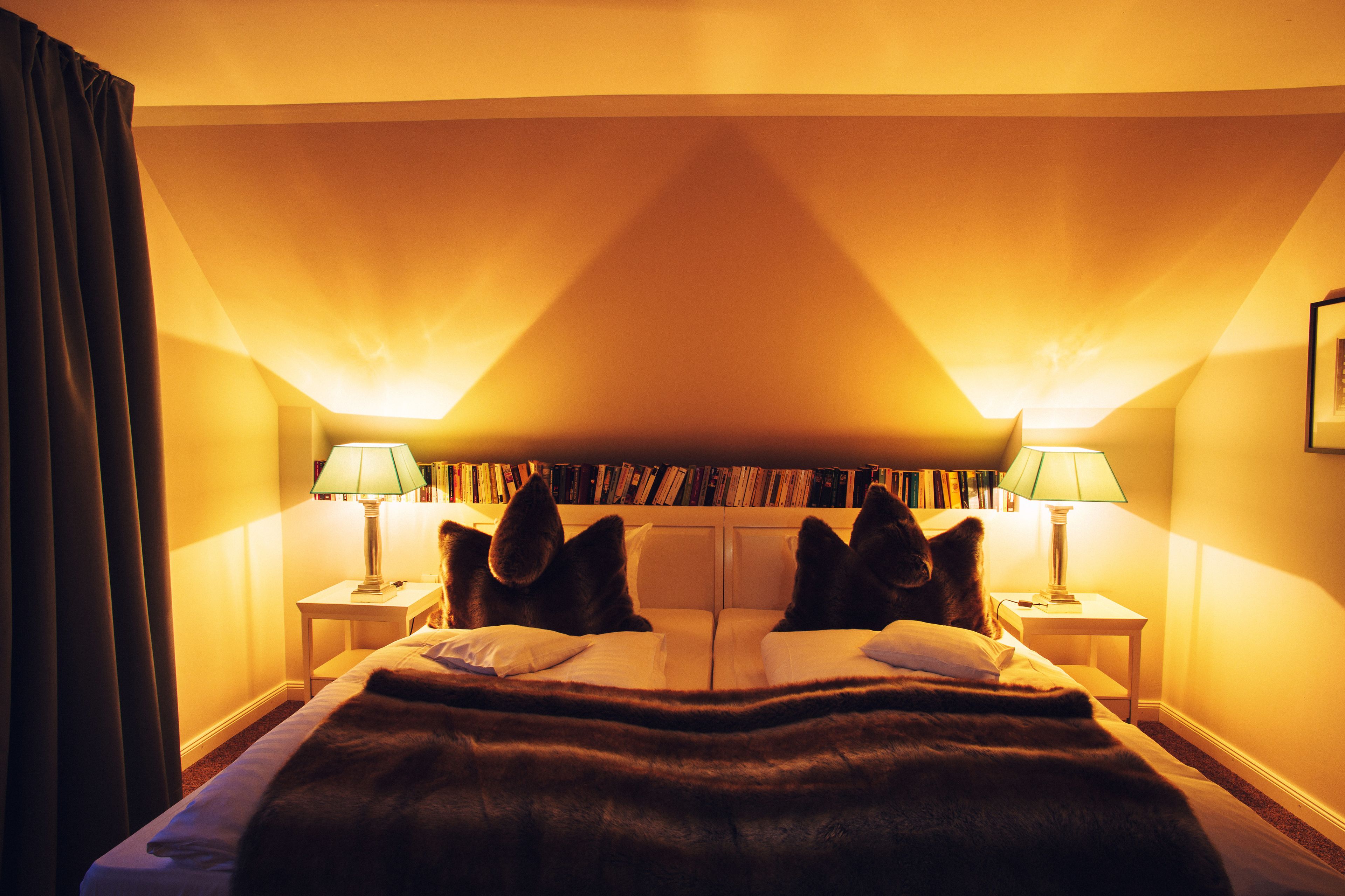 Ein Hotelzimmer mit einem Bett, zwei Nachttischlampen, einem Bücherregal und einem großen Fenster.
