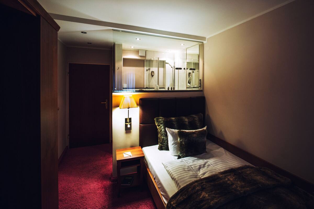 A hotel room with a bed, a nightstand, a mirror, and a view of the bathroom.