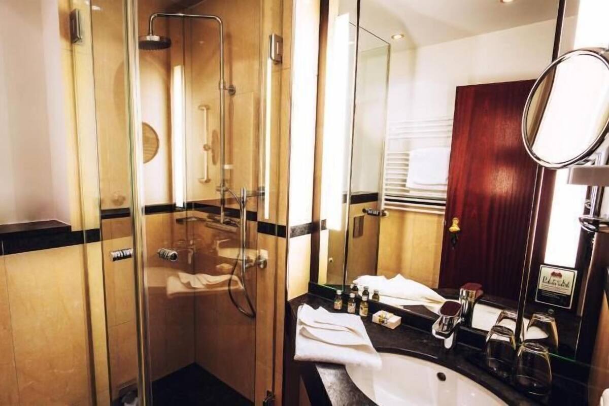 A hotel bathroom with a glass-enclosed shower, a sink with toiletries, and a mirror.