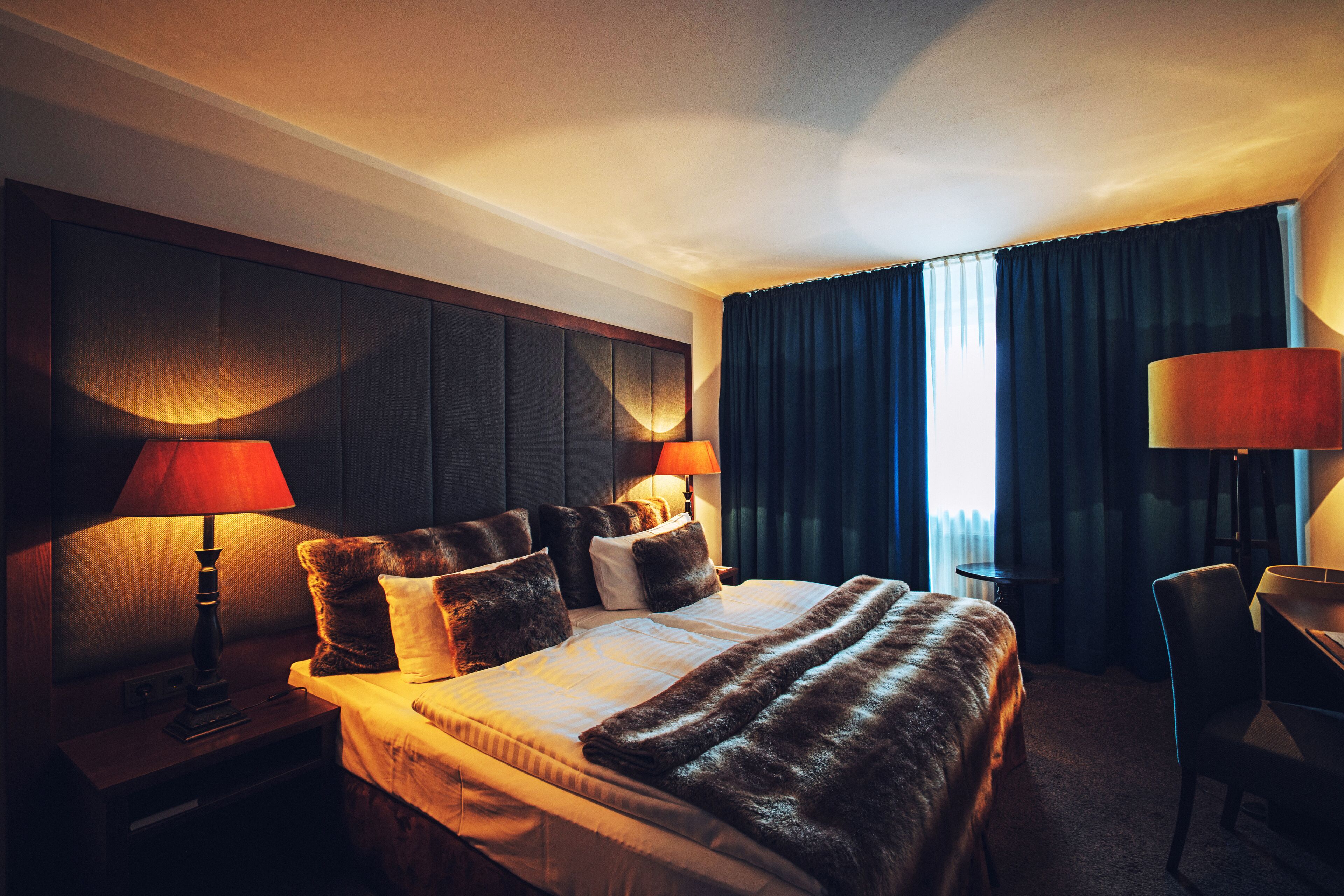 A hotel room with a large bed, two bedside lamps, a desk, and a chair.