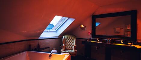 A bathroom with a skylight, a large mirror, a bathtub, and a vanity with a sink.